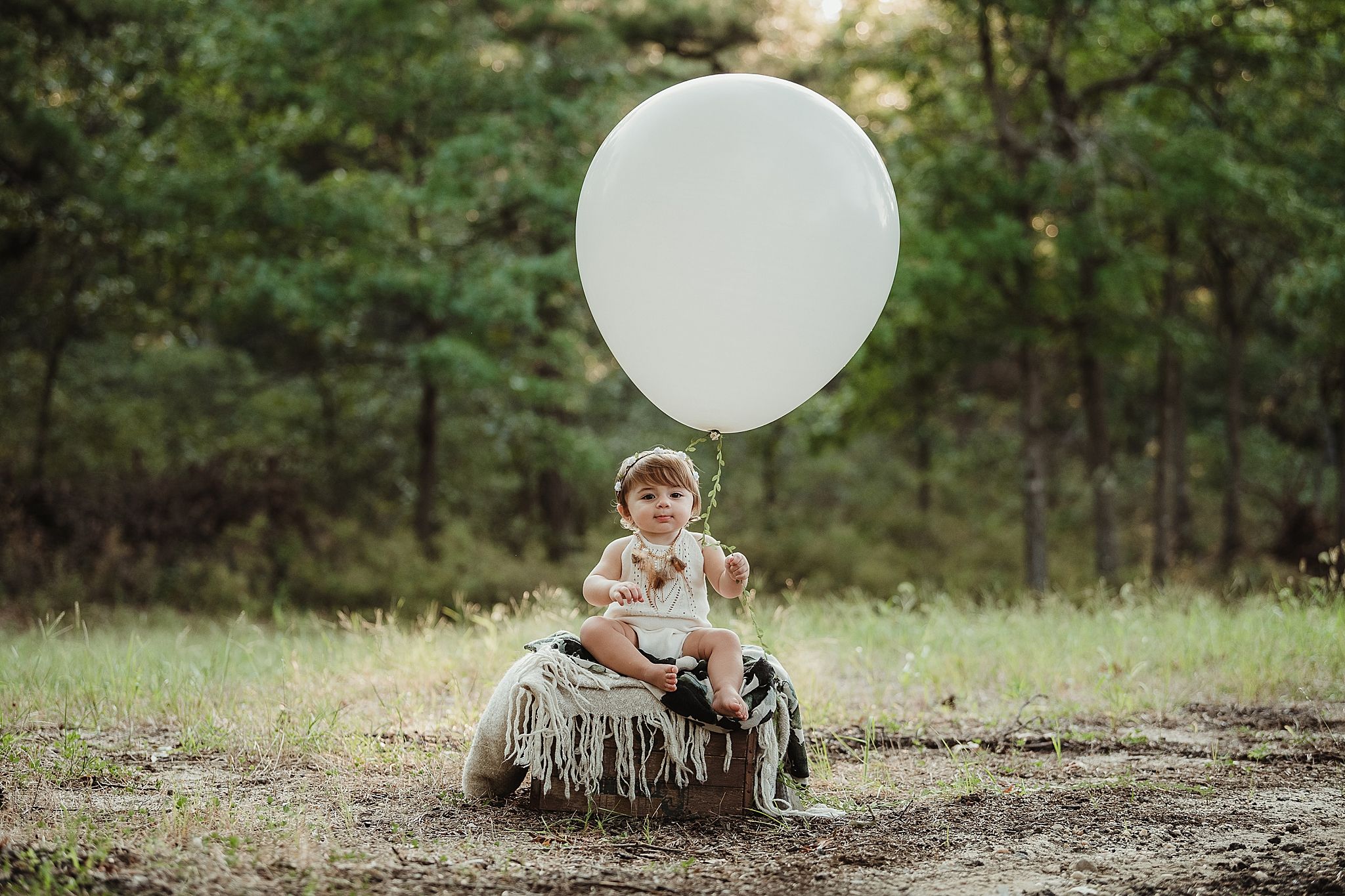 Outdoor portrait with white balloon and child sitting on rustic surface.