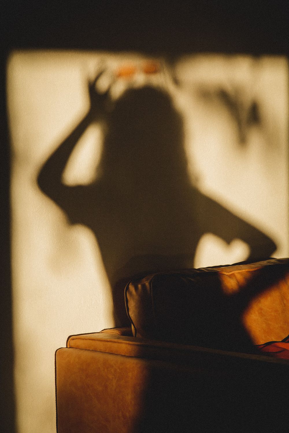 Dramatic silhouette cast on wall beside orange couch in moody lighting.