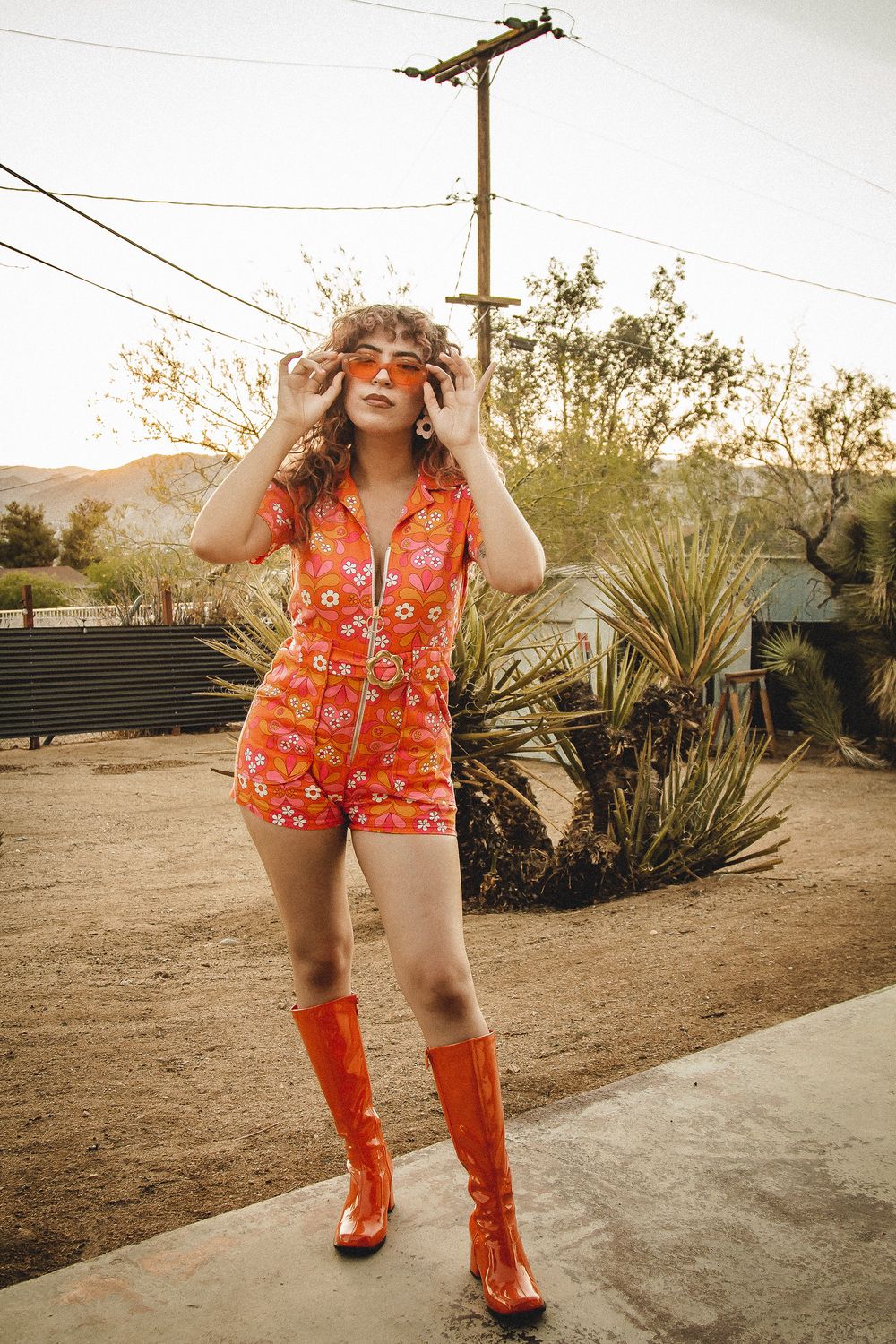 A playful desert photoshoot with a floral orange romper and matching knee-high boots against desert landscaping.