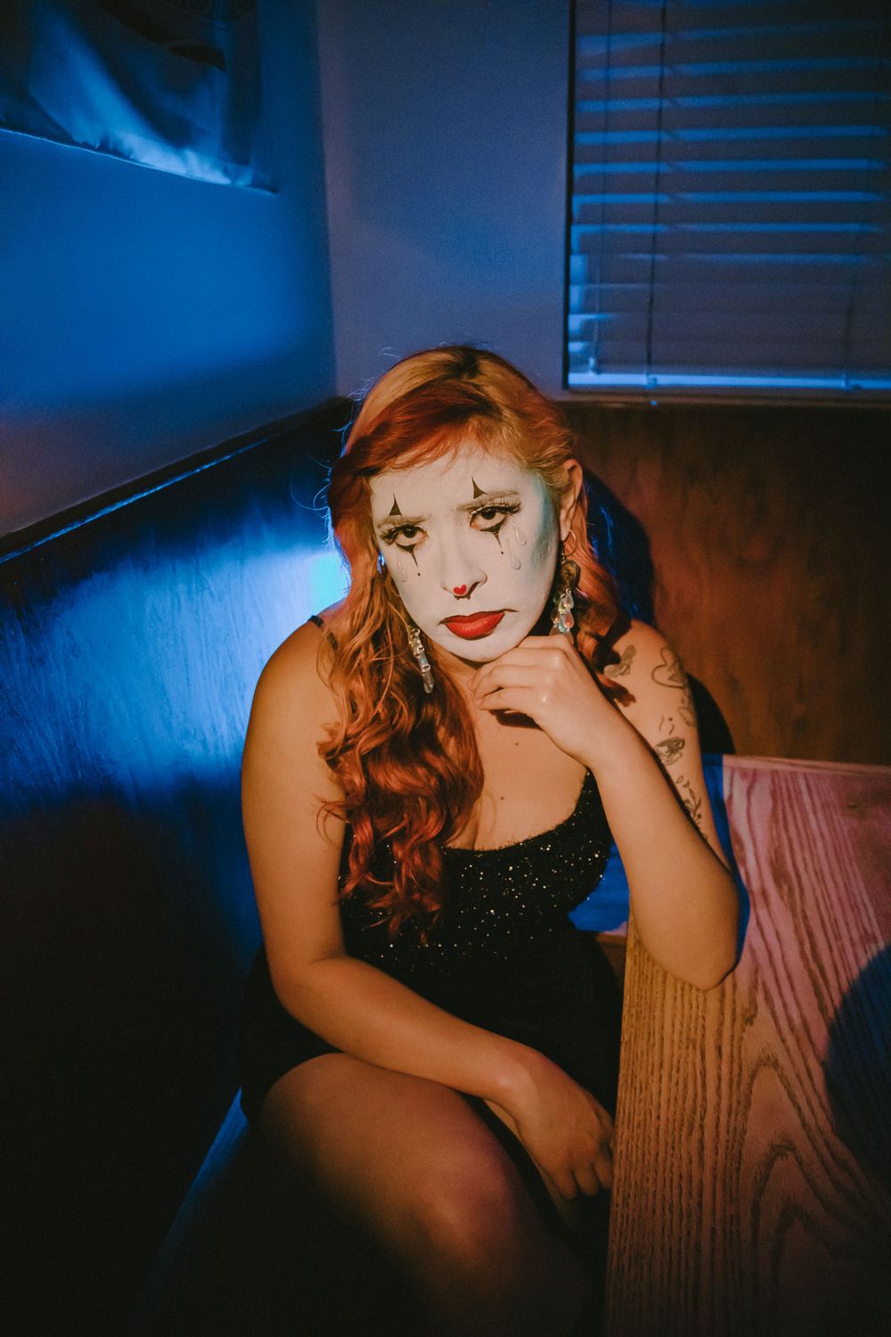 Artistic portrait on leather couch with dramatic makeup and tattoos in moody blue lighting.