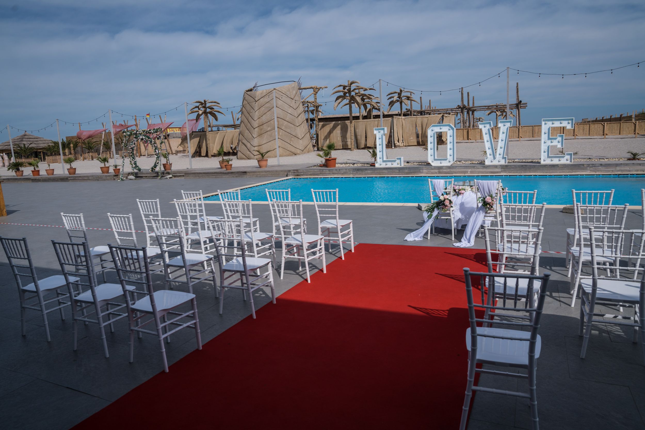 Beach wedding ceremony setup with white chairs and red carpet against ocean backdrop.