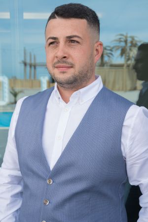 Person in gray vest and white shirt stands against modern glass building exterior.