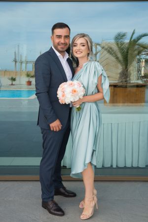 Couple in formal attire poses together at outdoor venue with mint green decor.
