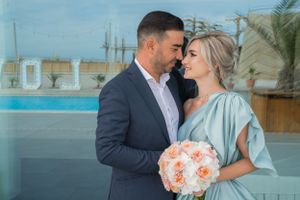 Romantic wedding photo of couple embracing at outdoor venue with tropical backdrop.