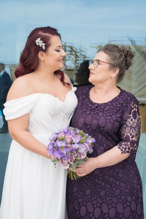 Emotional wedding moment between two people in white and purple dresses holding purple bouquets.