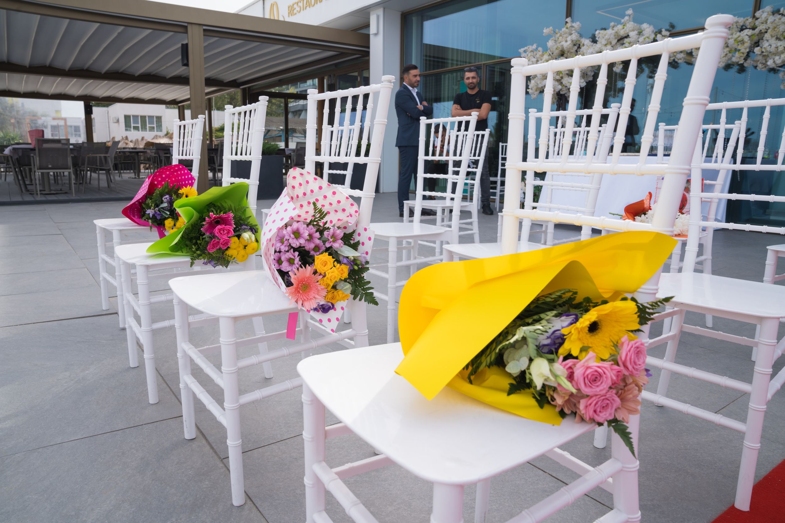 White rocking chairs line a porch decorated with colorful floral arrangements and yellow accents.