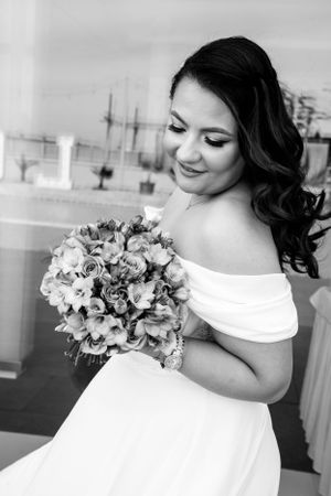 Black and white portrait of bride in off-shoulder dress holding floral bouquet.