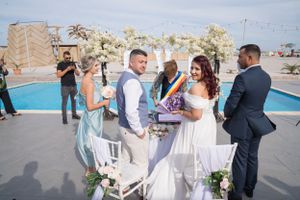 Wedding ceremony guests gather outdoors near a swimming pool on a sunny day.