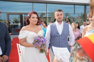 Wedding party members pose for photos outside contemporary building with red carpet.