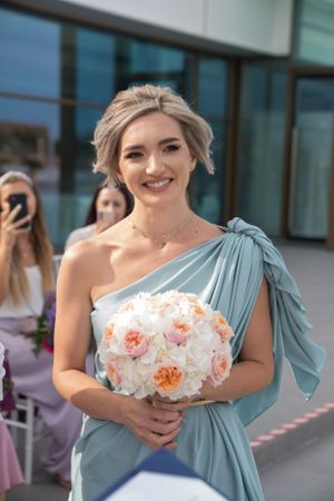 Bridesmaid in sage green dress holds peach and white bouquet.