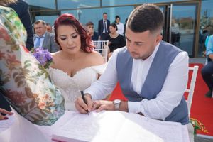 Wedding ceremony participants gathered around a table signing marriage documents outdoors.