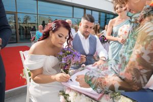 Wedding party signing official documents at an outdoor ceremony with floral decorations.