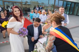 Wedding celebration outside glass building with guests and decorative flowers.
