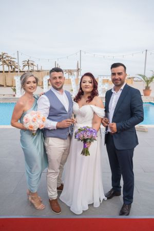 Wedding party poses together by a poolside venue with palm trees and string lights in the background.