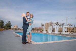 Scenic poolside wedding venue with palm trees and string lights under blue sky.