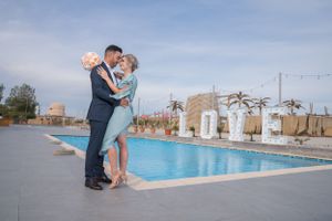 Romantic moment captured at poolside wedding venue with decorative lighting and palm trees.