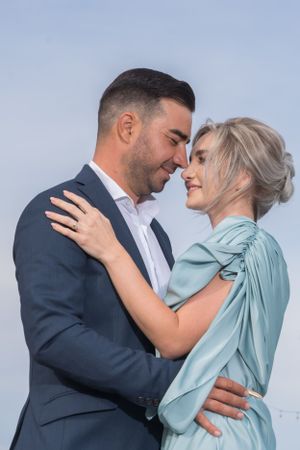 Close-up of romantic embrace between couple in formal attire against blue sky.