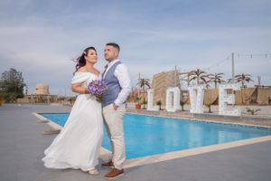 Wedding celebration by luxurious pool with palm trees and cabanas in background.