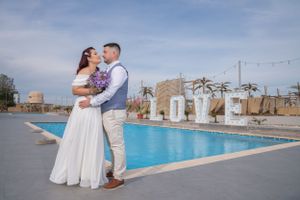 Romantic wedding photoshoot at resort pool with decorative palm trees and string lights.