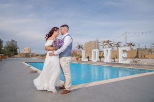 Wedding couple shares special moment by resort pool with palm trees in background.