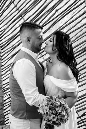 Black and white wedding photo of couple sharing romantic moment against bamboo wall.
