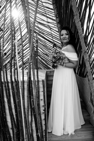 Black and white portrait of bride with bouquet among palm fronds.