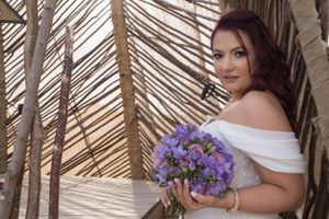 Bride with burgundy hair holds purple bouquet against rustic bamboo setting.
