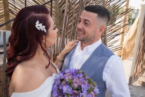 Wedding couple shares tender moment with purple bouquet against bamboo backdrop.