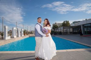 Panoramic wedding photography showcasing a couple by a luxurious pool with white columns.
