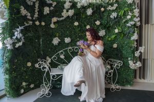 Wedding portraits captured against a lush green floral wall backdrop with decorative white elements.