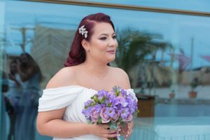 Bride with burgundy hair poses with purple bouquet against modern glass building backdrop.