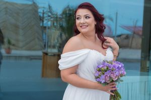 Bride holding purple orchid bouquet smiles during outdoor wedding photoshoot.