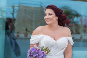 Bride with flowing white dress poses with purple bouquet against modern architecture.