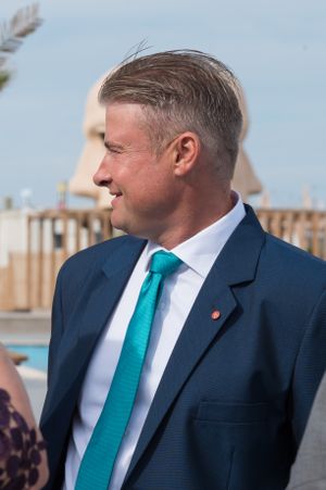 Groom in navy suit with teal tie smiles during outdoor beach wedding.