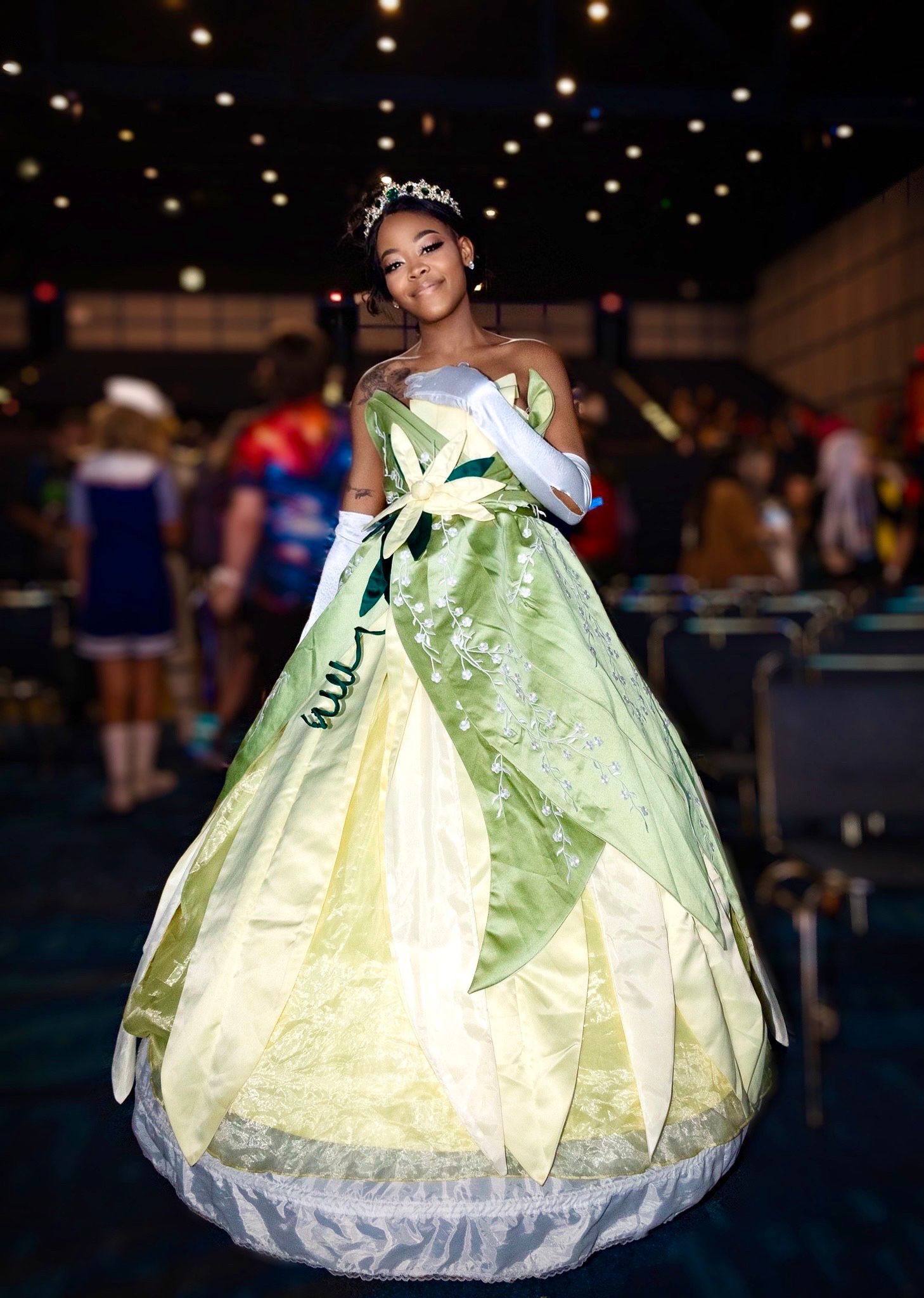 Cosplayer wearing elegant light green ballgown poses in convention hall setting.