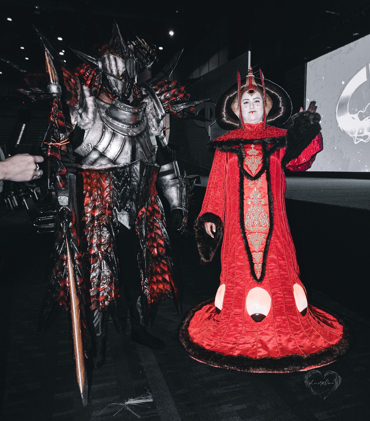 Dark fantasy cosplay featuring imposing armored warrior and regal red-robed figure at convention.