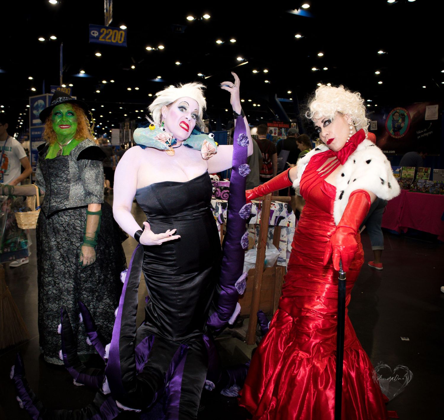 Group of cosplayers in formal evening gowns pose together under convention center lighting.