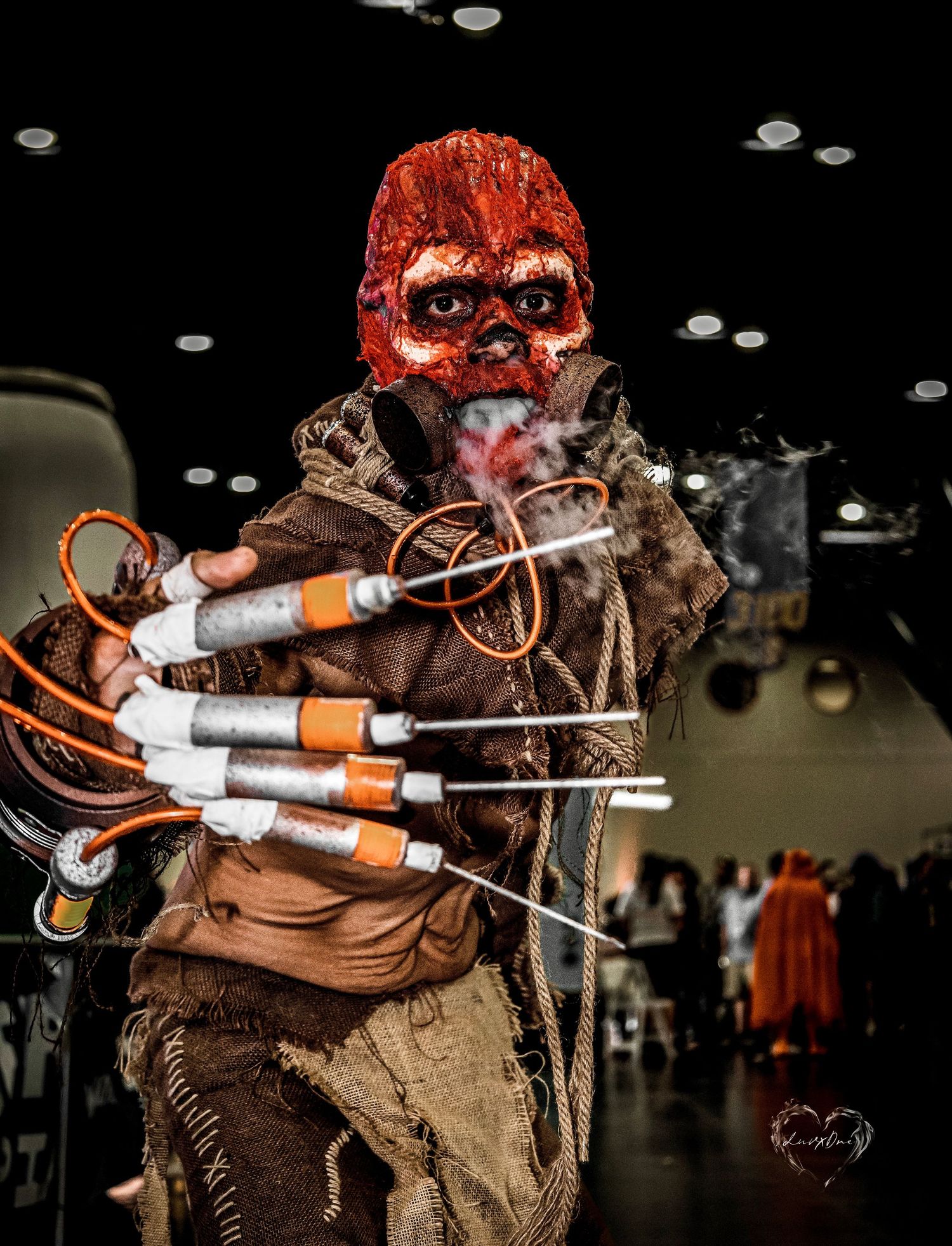 Post-apocalyptic cosplayer with red mask and multiple improvised explosive props at convention.