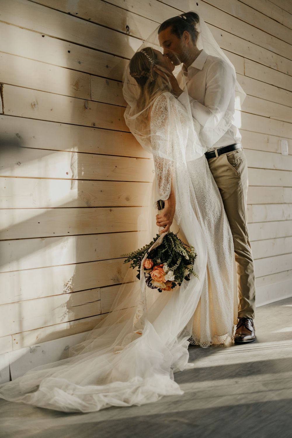 A tender moment between newlyweds against rustic wooden walls with peach roses.