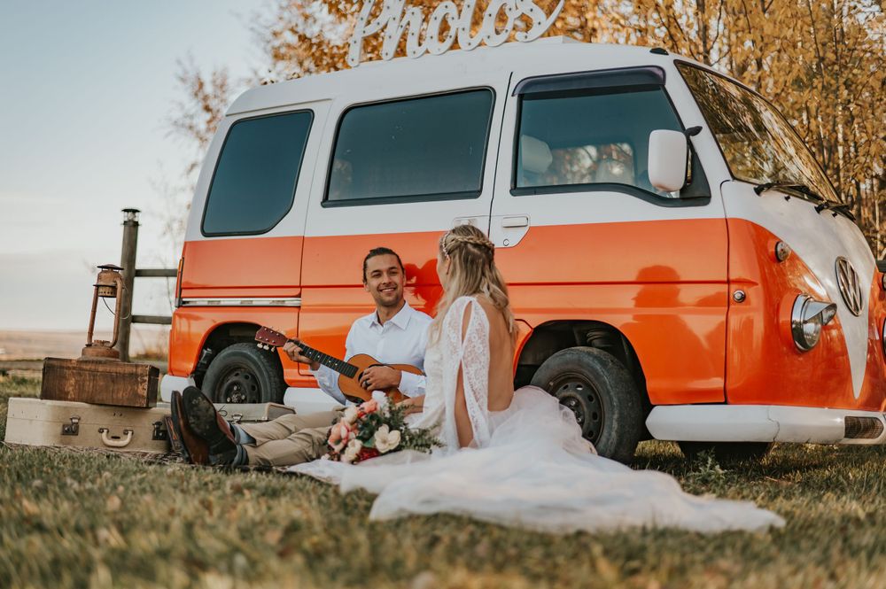 Wedding picnic scene with retro orange and white van in a sunny meadow.