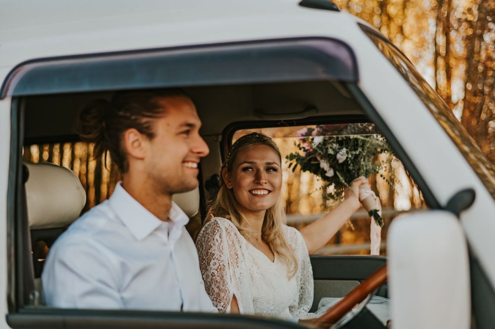 Wedding couple smiles inside vintage van during golden hour photoshoot.