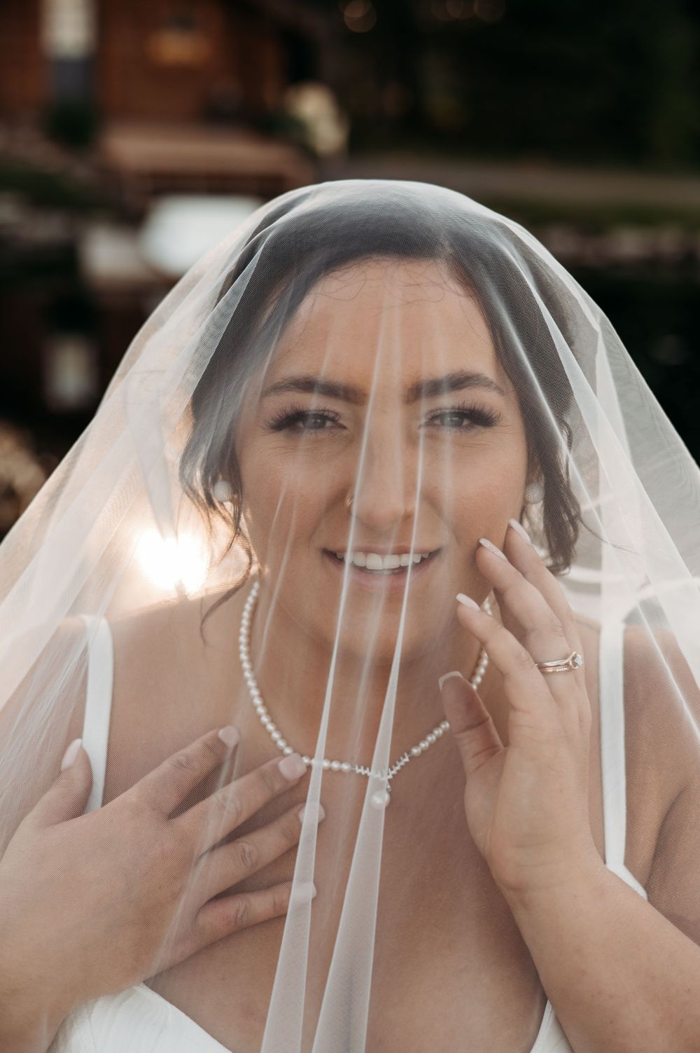 A delicate bridal portrait through a sheer veil showcasing pearl jewelry and natural makeup.