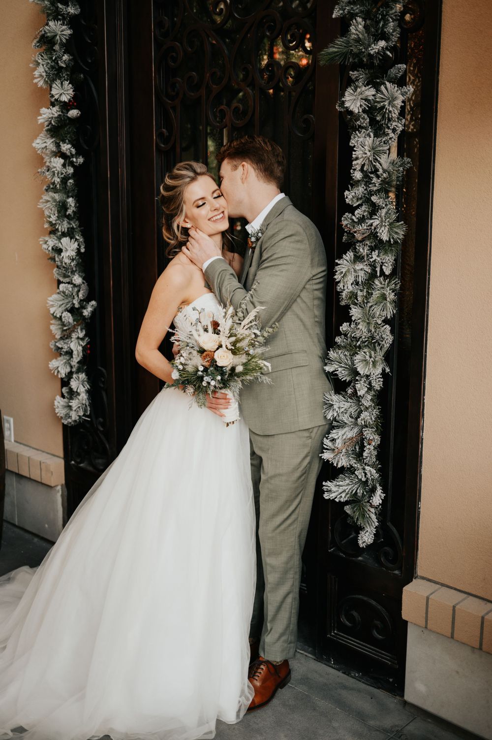 Elegant wedding portrait of couple in front of ornate doorway with floral decorations.