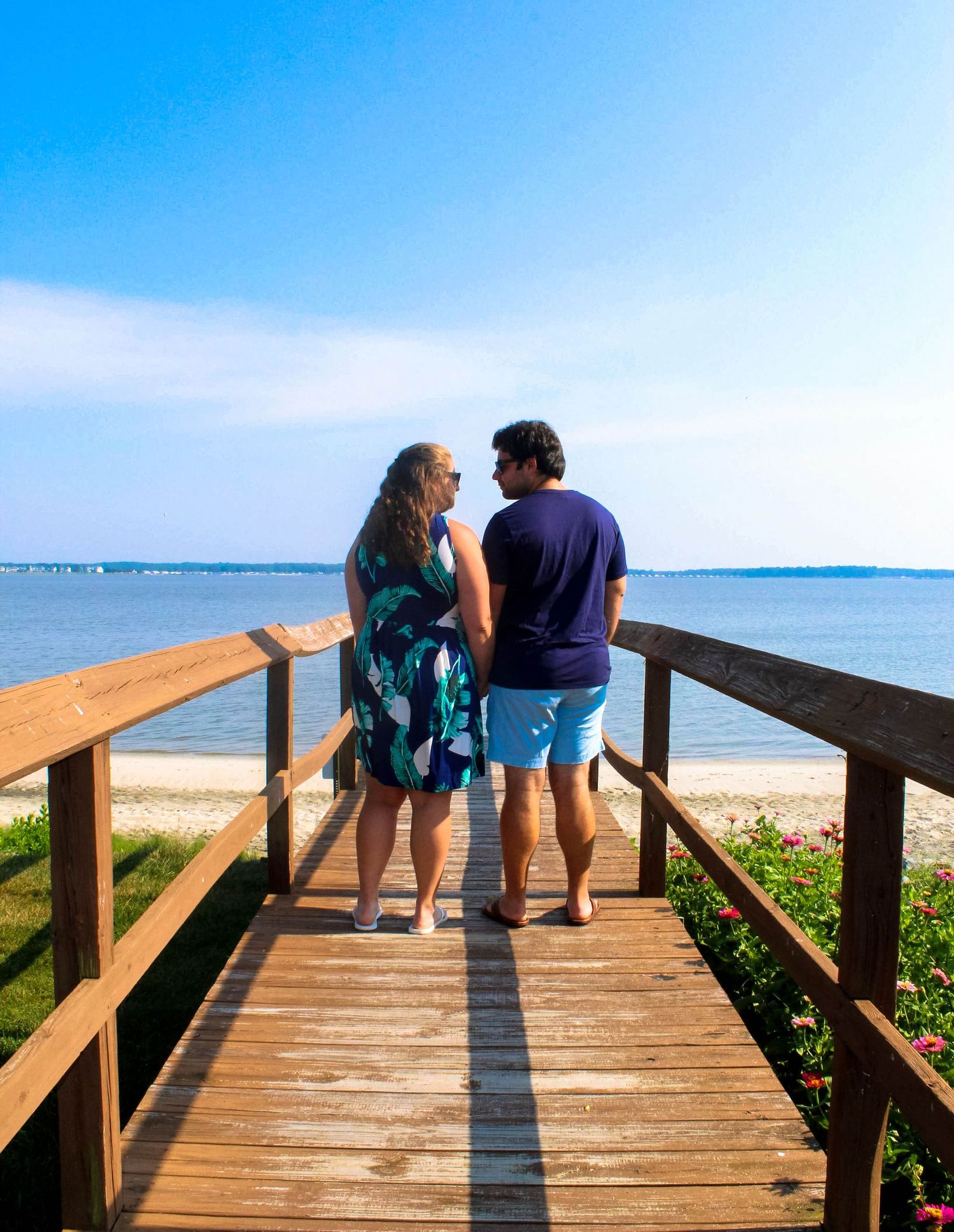 Couple standing together on wooden boardwalk overlooking ocean view.