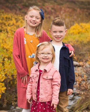 Group poses together outdoors with autumn foliage and rocks in background.