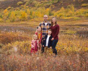 Family poses together in autumn field with golden foliage in background.