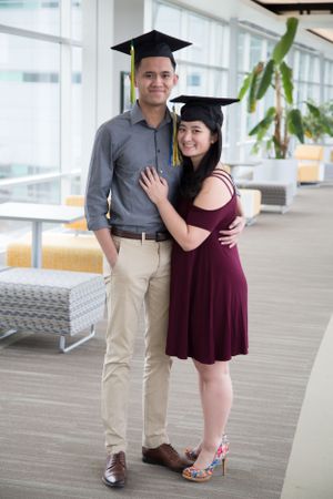 Graduation photo with person in burgundy dress and cap posing indoors.
