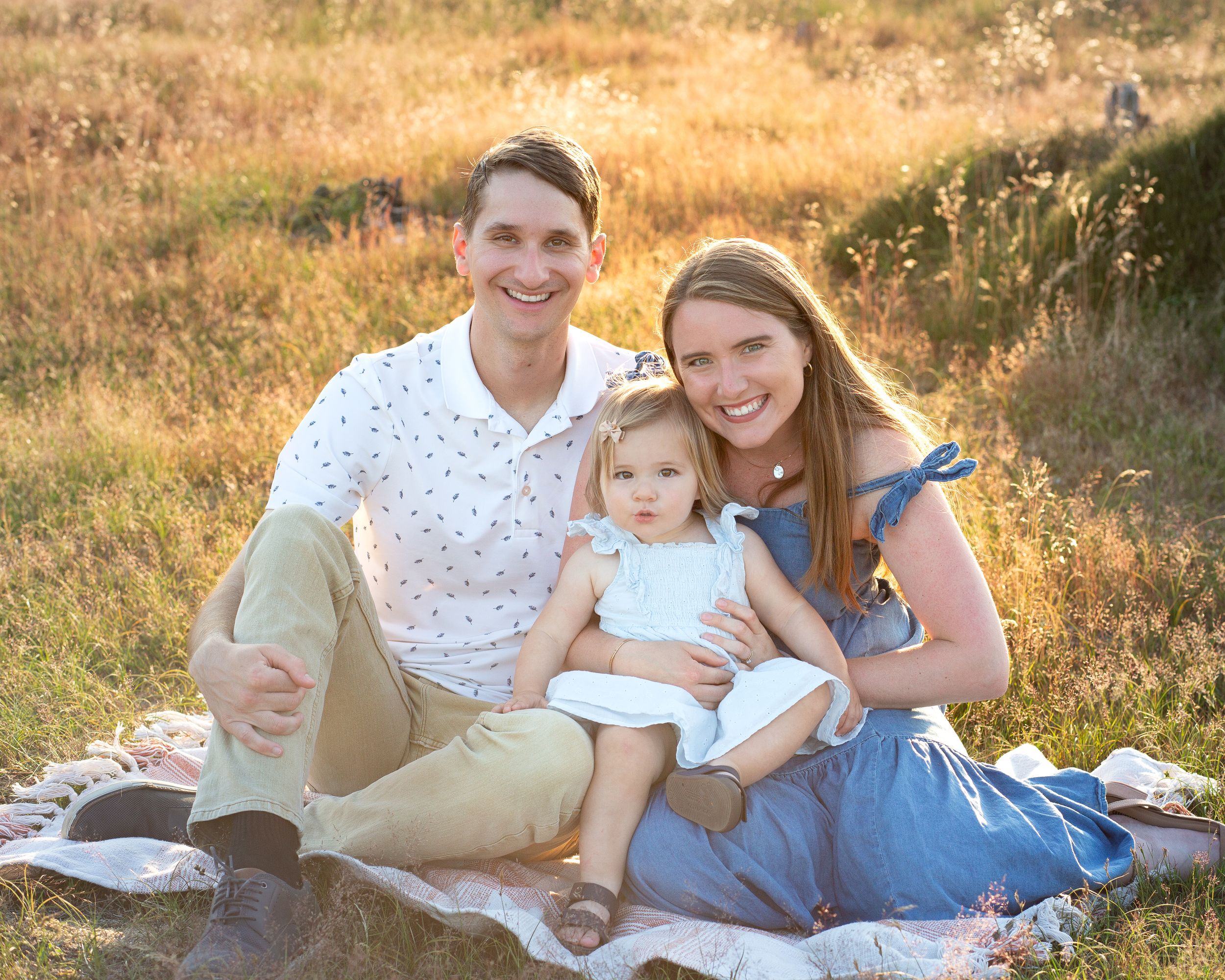 Family relaxing on a picnic blanket in a golden field at sunset.