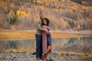 Couple sharing romantic moment by scenic mountain lake with autumn foliage in background.