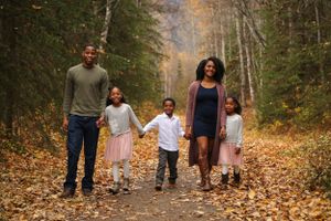 Family walking together on leaf-covered forest trail during fall season.